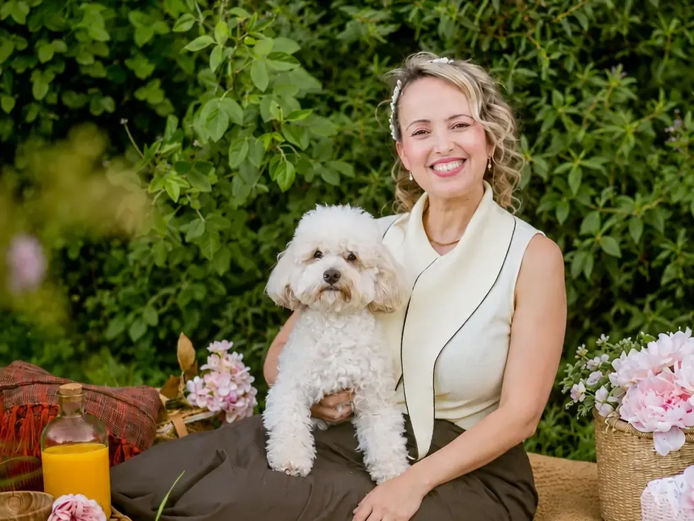 Yaiza smiling as she sits on a picnic blanket in a garden, with Tuililin, a white maltipoo, on her lap